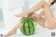 A woman sitting on the floor next to a watermelon.