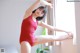 A woman in a red leotard is posing by a window.